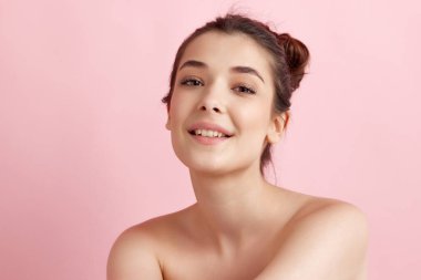 Nazik, güzel, çıplak omuzlu, bakımlı, pürüzsüz, sağlıklı ciltli, pembe arka planda kameraya bakan genç bir kadın. Doğal kadın güzelliği kavramı, vücut ve cilt bakımı, kozmetoloji, sağlık, reklam