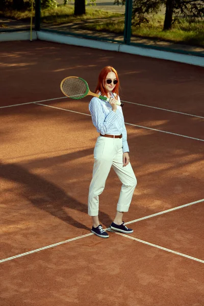 身穿时髦休闲装 戴着太阳镜 头戴红头发的年轻女子在露天网球场摆姿势的全长头像 体育概念 积极的生活方式 业余爱好 休闲时尚 闲暇时间 — 图库照片