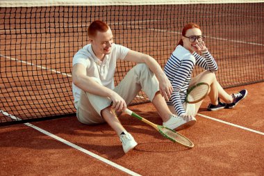 Mutluluk. Gündüz vakti tenis raketiyle poz veren yakışıklı genç bir adam ve şık giyimli güzel bir kadın. Günlük moda, spor, aktif yaşam tarzı, hobi, boş zaman kavramı, reklam