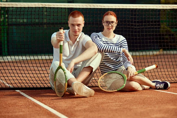 年轻英俊的男子和漂亮的女子 穿着休闲时髦的衣服 白天在球场上摆出网球拍的姿势 休闲时尚 积极的生活方式 业余爱好 闲暇时间 广告的概念 — 图库照片