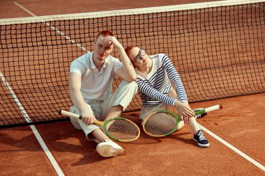 Gündüz vakti tenis raketiyle poz veren yakışıklı genç bir adam ve şık giyimli güzel bir kadın. Günlük moda, spor, aktif yaşam tarzı, hobi, boş zaman kavramı, reklam