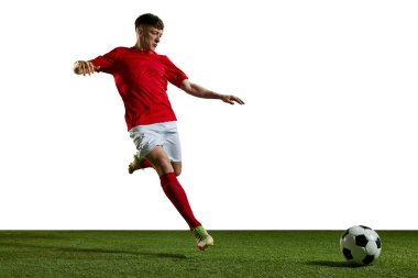 Kırmızı üniformalı genç bir adam, hareketli bir futbolcu, beyaz arka planda top oynuyor, tekmeliyor. Profesyonel spor, eylem, yaşam tarzı, rekabet, hobi, eğitim, reklam kavramı