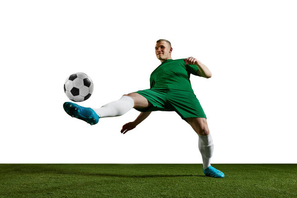 Concentrated young man, football, soccer player in uniform training, kicking ball with leg against white background. Concept of professional sport, action, lifestyle, competition, hobby, training, ad