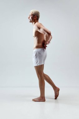 Gri stüdyo arka planına karşı iç çamaşırlarıyla poz veren kaslı, yakışıklı, şık bir adamın tam boy görüntüsü. Erkek doğal güzellik kavramı, vücut bakımı, sağlık, spor, moda, reklam