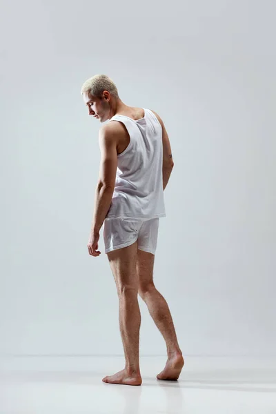 Comfort look. Full-length image of young handsome man with muscular body posing in underwear and singlet against grey studio background. Concept of male natural beauty, body care, health, sport, ad