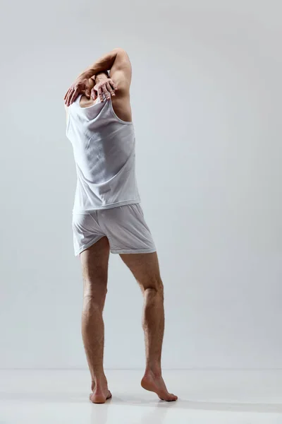 Comfort look. Full-length image of young handsome man with muscular body posing in underwear and singlet against grey studio background. Concept of male natural beauty, body care, health, sport, ad