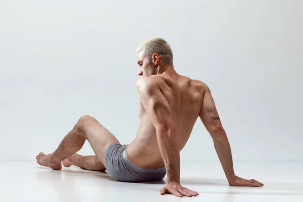 年轻英俊男子 肌肉发达 轻松自在 体格强壮 身穿内衣 在灰色工作室背景下躺在地板上 男性自然美 身体护理 广告等概念 — 图库照片