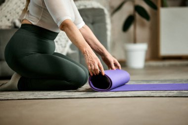 Deri taytlı ve tişörtlü son sınıf bayan evde antrenman için hazırlanıyor, fitness matt oynuyor. Vücudunu formda tut. Sportif ve sağlıklı yaşam tarzı kavramı, yaş, vücut bakımı, spor, sağlık.