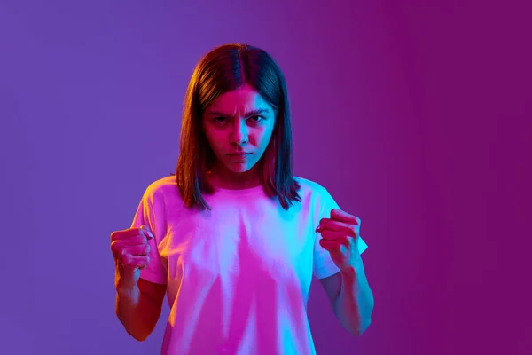穿着休闲装的少女的画像 表情严肃地站着 在霓虹灯下的紫色背景上方举起拳头 生活方式 广告的概念 — 图库照片