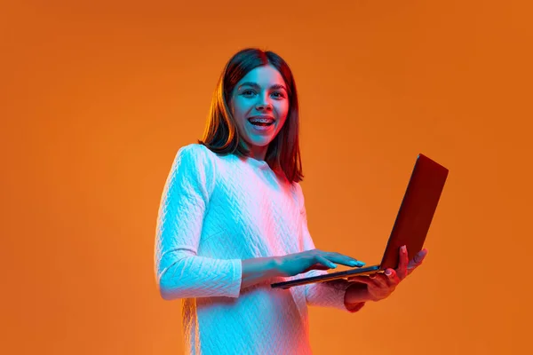 아름답고 웃으며 노트북을 공부하고 빛으로 주황색 스튜디오 배경에 대항하는 인간의 — 스톡 사진