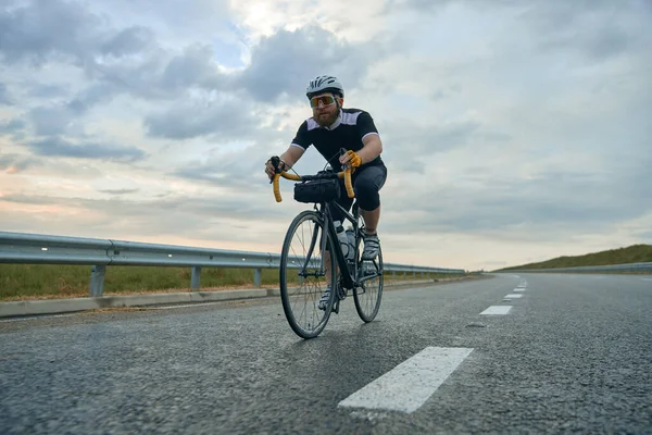 Динамічне Зображення Юного Бородатого Спортсмена Велосипедиста Шоломі Порожній Дорозі Ввечері — стокове фото