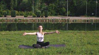 Rahatlama. Genç sportif kız gölün yakınındaki çimlerde spor salonunda oturuyor, dışarıda yoga yapıyor ve meditasyon yapıyor. Sağlıklı ve sportif yaşam tarzı, vücut bakımı, aktif yaşam kavramı