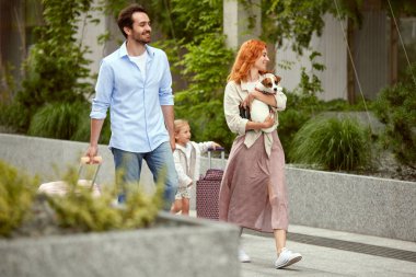 Güzel genç bir çift, gülümseyen adam ve kadın küçük kızı ve köpeğiyle yaz tatiline çıkıyorlar. Sokakta yürüyen insanlar. Aile kavramı, çocukluk ve ebeveynlik, seyahat, tatil