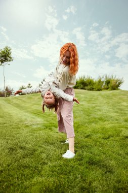 Neşeli hafta sonları. Güzel kızıl saçlı genç bir kadın, annesi sıcak bir yaz gününde küçük kızıyla parkta oynuyor. Aile kavramı, çocukluk ve ebeveynlik, eğlence, hafta sonları, aşk, reklam