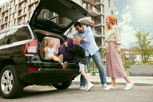 stock image Young happy couple, family, man and woman gong on summer trip on car with the little children. Man putting suitcases into car. Concept of family, childhood and parenthood, travelling, vacation, ad