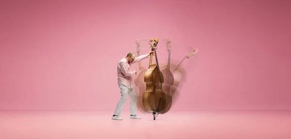 創造的なコラージュ ピンク色のスタジオを背景にダブルベースを演奏スタイリッシュな口ひげを持つ才能 感情的な若い男 エンターテイメント フェスティバル パフォーマンス 広告の概念 — ストック写真