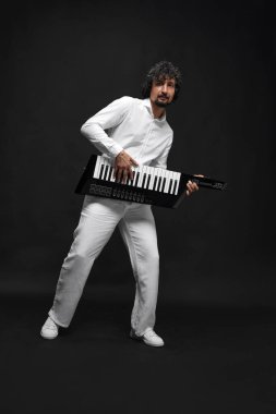 Beyaz takım elbiseli şık sakallı bir adamın sentezleyici çalarkenki görüntüsü. Kablosuz keytar, siyah stüdyo arka planında. Müzik kavramı, yetenek, hobi, eğlence, festival, performans, reklam