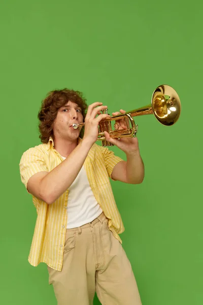 巻き毛の若い男の肖像 緑のスタジオの背景にトランペットを演奏才能のあるミュージシャン エンターテイメント フェスティバル パフォーマンス 広告の概念 — ストック写真