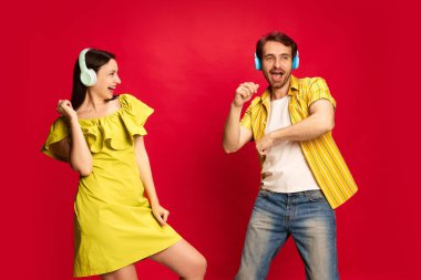 Parlak sarı elbiseli genç adam ve kadın kulaklıkla müzik dinliyor ve kırmızı stüdyo arka planında dans ediyorlar. Arkadaşlık kavramı, ilişki, iletişim, duygular, yaşam tarzı