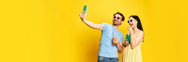 夏休み カップル 男性と女性がサングラスをかけてレモネードを飲み 黄色のスタジオを背景に自撮りします コミュニケーション ライフスタイルの概念 — ストック写真