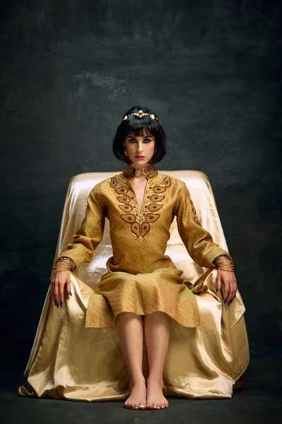 クレオパトラのイメージで美しい若い女性の肖像画 暗いヴィンテージの背景に座ってエレガントな金のドレスで女王 アンティーク文化 広告コンセプトの比較 — ストック写真