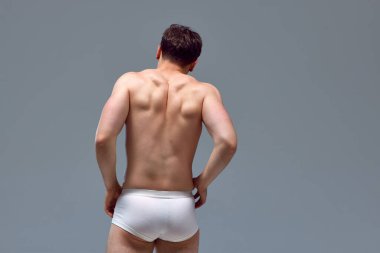 Kaslı, rahatlamış erkek siyahın arka görünüşü. Gri stüdyo geçmişiyle iç çamaşırsız poz veren bir adam. Omurga sağlam. Erkeklerin güzellik anlayışı, sportif ve sağlıklı yaşam tarzı, atletik vücut