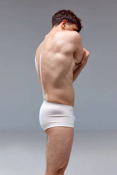 背痛年轻男子 身强体壮 身披便衣 背对灰色工作室背景 男人的美 医学概念 — 图库照片