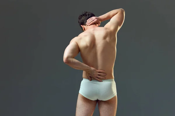 颈部和脊椎疼痛 截断了肌肉的男性形象 松驰了背 在灰色工作室背景下穿着内裤的男人 男人美的概念 运动健康的生活方式 运动的身体 — 图库照片