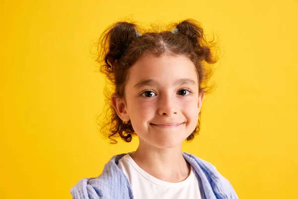 漂亮小女孩的特写 头发卷曲的孩子摆姿势 看着相机 在黄色的摄影棚背景下微笑 情感概念 生活方式 — 图库照片
