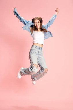 Genç ve güzel bir kızın tam boy portresi, günlük giysiler içindeki öğrenci pembe stüdyo arka planında neşeyle zıplıyor. Mutluluk. İnsan duyguları kavramı, moda, gençlik, yaşam tarzı, güzellik, reklam
