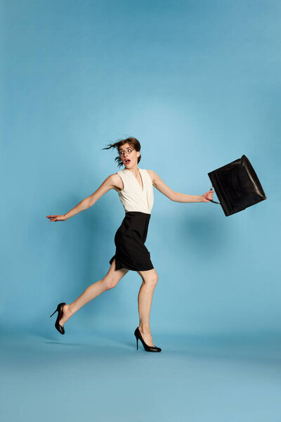 Deadlines. Business Woman, office worker, running with briefcase from burning projects against blue studio background. Concept of human emotions, business, education, success, lifestyle, ad