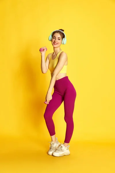 スポーツウェアやヘッジの若いスリム女性のフル長さのイメージ 黄色のスタジオの背景に対するダンベルとトレーニング スポーツ フィットネス ボディケア ファッション ライフスタイル 広告の概念 — ストック写真