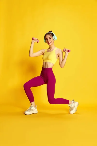 身穿运动服和树篱的年轻苗条女子的全长形象 带着黄色背景的哑铃训练 身体护理 生活方式 广告等概念 — 图库照片