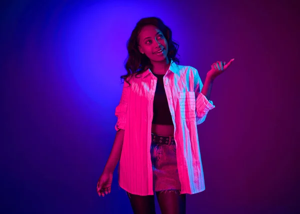 在霓虹灯下 年轻迷人的非洲女子身穿白衬衫 面容梦幻 背景为渐变蓝色紫色的肖像 人类情感 生活方式 广告的概念 — 图库照片