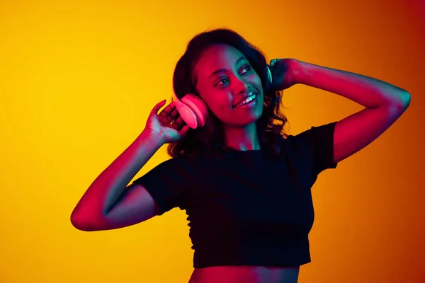 在霓虹灯下 年轻美丽的非洲女人用耳机在黄色工作室背景下听音乐的肖像 享受快乐 人类情感 生活方式 广告的概念 — 图库照片