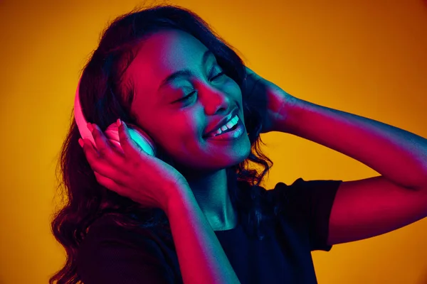 年轻美丽的非洲女人的肖像 她在耳机里听音乐 在霓虹灯下享受着黄色的工作室背景 人类情感 生活方式 广告的概念 — 图库照片