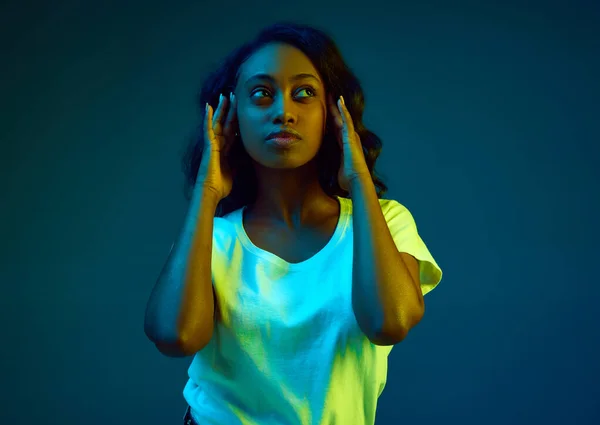 穿着白色T恤的年轻非洲女人的画像 面对霓虹灯下的青色 蓝色背景 摆出一副深思熟虑 专注的样子 人类情感 生活方式 广告的概念 — 图库照片