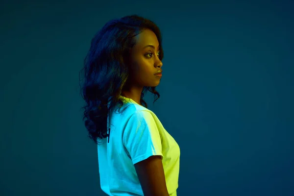 漂亮的年轻非洲女人穿着白色T恤 在霓虹灯下与青色 蓝色的工作室背景相对照的肖像 人类情感 生活方式 广告的概念 — 图库照片