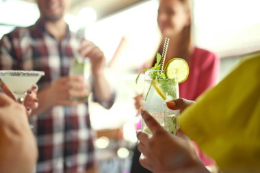 Kadehle içki ve mojito içen kadın eli yakın plan. İnsanlarla geçmişi bulanık. Arkadaş toplantısı. Arkadaşlık kavramı, toplantı, eğlence, iletişim, alkol içecekleri