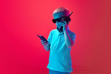 Küçük çocuk, çocuk retro 'da konuşuyor, eski cep telefonu pembe stüdyo arka planına karşı neon ışıkta. Ciddi bir bakış. Çocukluk kavramı, yaşam tarzı, duygular, eğitim, moda, bakım, reklam