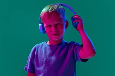 Çocuk, küçük çocuk kulaklıkla müzik dinliyor. Cyan stüdyosunun arka planında, neon ışıkta. Hoş olmayan, kötü ses, ses. Çocukluk kavramı, yaşam tarzı, duygular, eğitim, moda, bakım, reklam