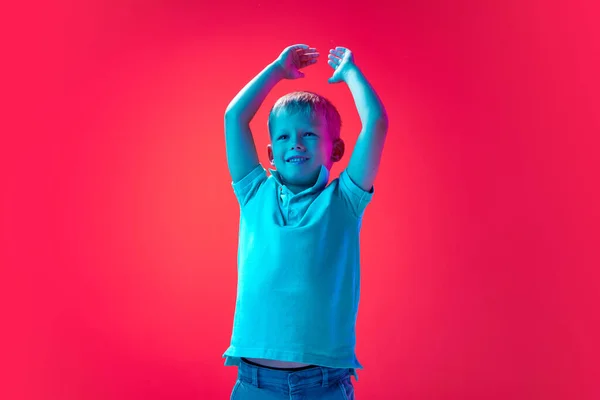笑顔の男の子の肖像画 子供の手を上げて ネオンの光の中でピンクのスタジオの背景に興奮と幸せを感じる 子供時代 ライフスタイル ファッション 広告の概念 — ストック写真