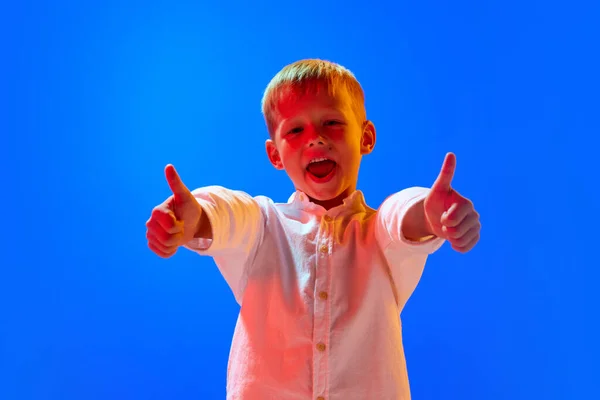 Portrét Pozitivního Chlapečka Bílém Tričku Úsměvem Modrém Pozadí Studia Neonovém — Stock fotografie