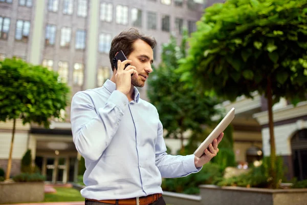 Young Businessman Standing Office Outdoors Looking Tablet Talking Mobile Phone — Stock Photo, Image