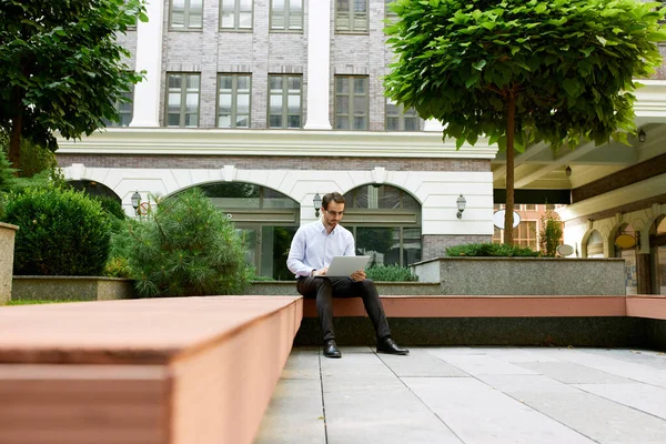 Empresário Sério Concentrado Trabalhando Online Com Laptop Sentado Banco Lado — Fotografia de Stock