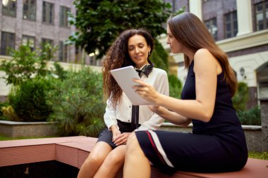 İş kadını ofisin dışında bankta oturuyor, tablete bakıyor ve konuşuyor. Müşteri ve sanatçı işbirliği. İş kavramı, kariyer gelişimi, hırslar, başarı, ofis yaşam tarzı