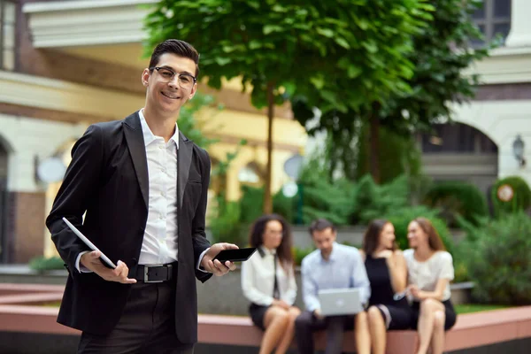 Focus Smiling Confident Businessman Standing Laptop Mobile Phone Office Blurred — Stock Photo, Image