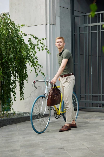 自転車で近代的な建物の近くに立ってスマートカジュアル服でハンサムな スタイリッシュな若いビジネスマン 仕事に行く ビジネス アクティブライフスタイル ファッション 生態学の概念 — ストック写真