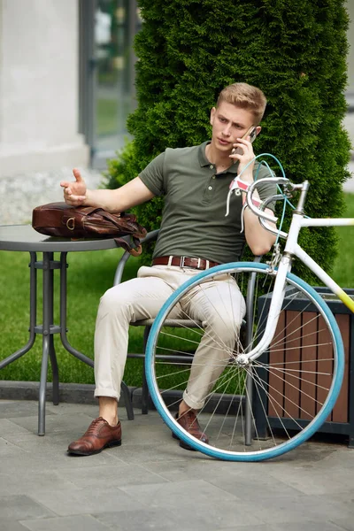 スタイリッシュな ハンサムな 深刻なビジネスマンのベンチに座って 携帯電話で話しています 自転車で仕事に行く ビジネス課題の解決 ビジネス アクティブライフスタイル ファッション 生態学の概念 — ストック写真