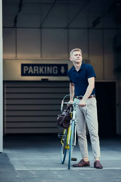 駐車場 ハンサムな若いビジネスマン スタイリッシュな服の従業員は自転車で仕事に行く 近代的な建物の外観 ビジネス アクティブライフスタイル ファッション 生態学の概念 — ストック写真